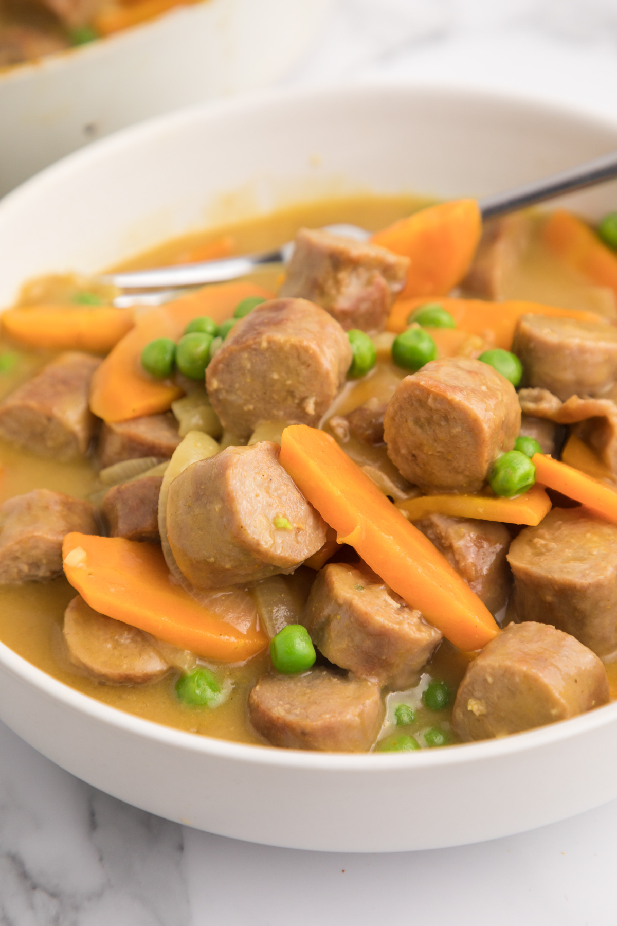 Close up images of curried sausages in white bowl.